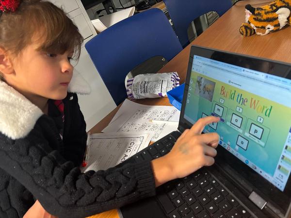 A girl interacting with a laptop, engaged in a learning activity at a table.