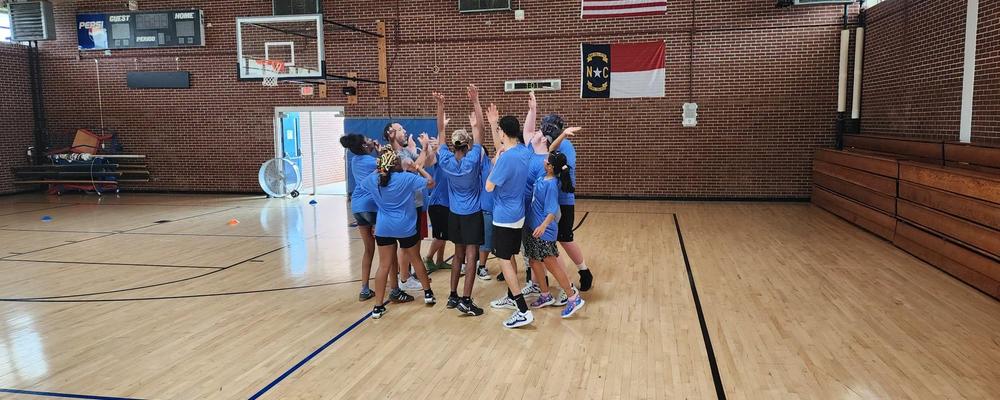 A group of teenagers celebrating in a gym with flags on the wall.