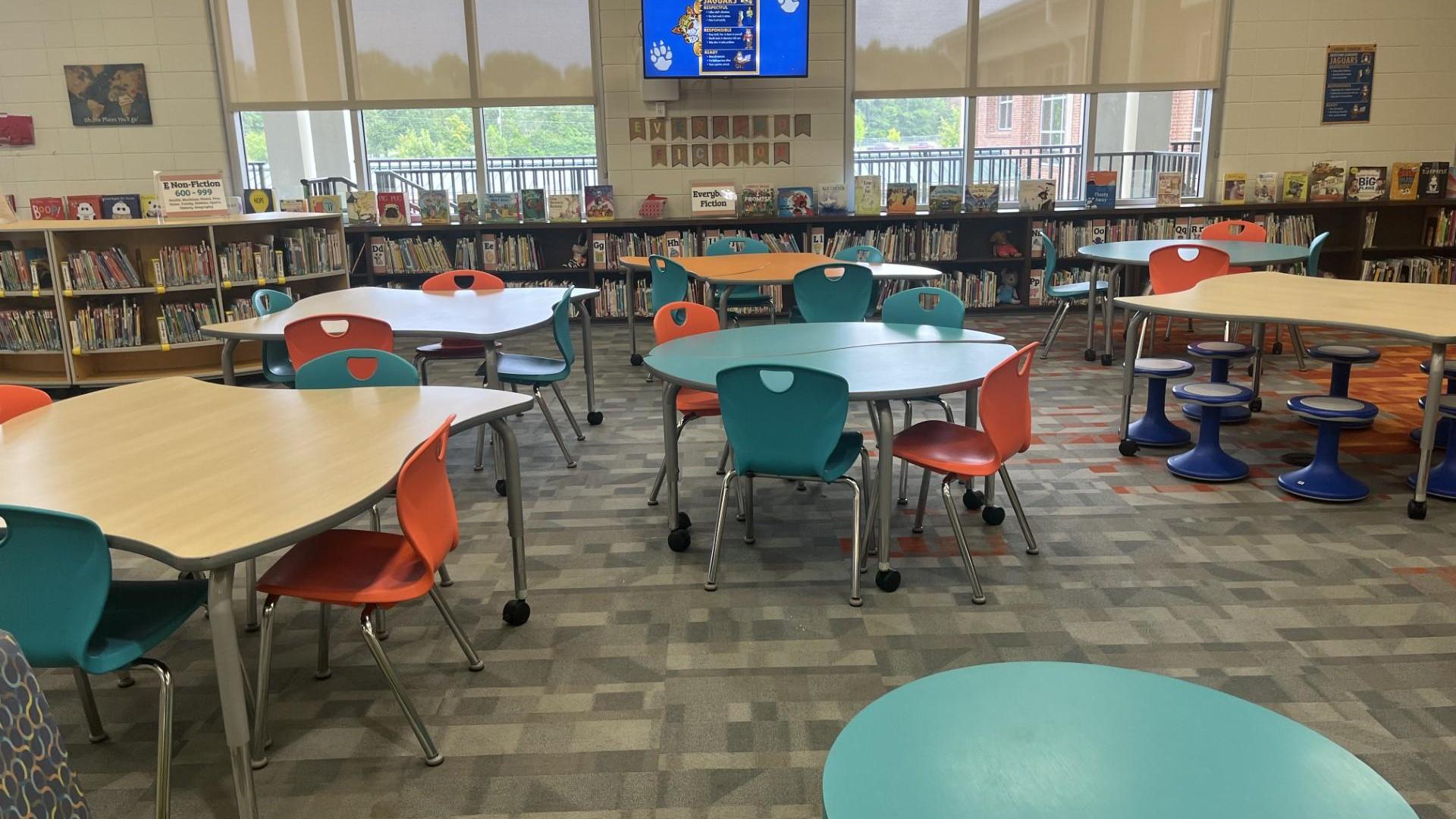 Bright library with colorful tables and a digital screen in an open area.