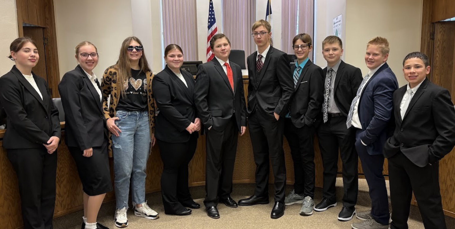 Students dressed formally pose together in a courtroom setting.