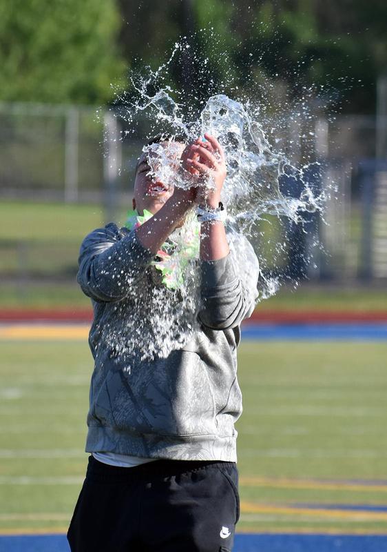 Person in a gray sweatshirt splashes water in the air, wearing a floral lei on a field.