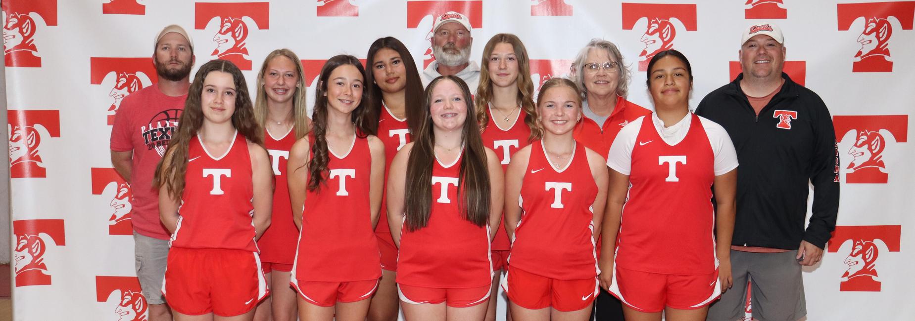 A group of girls in red sports uniforms posing with coaches against a branded backdrop.