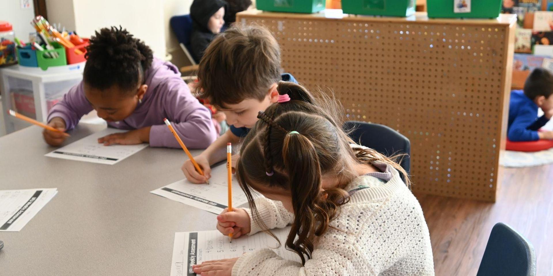 Children focused on writing assignments at a classroom table.