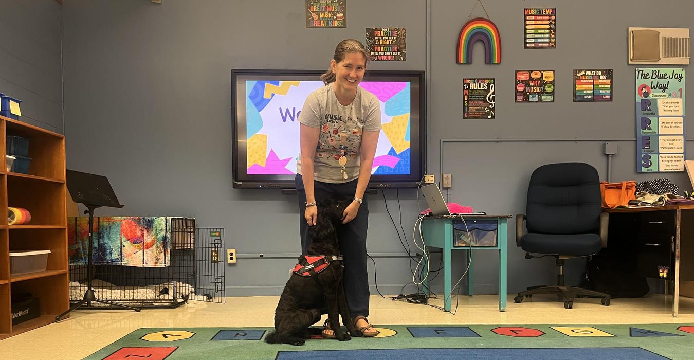 A woman standing with a dog in a classroom setting with colorful decor.