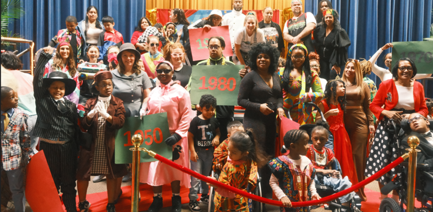 A diverse group of adults and children posing with year signs in front of a stage.