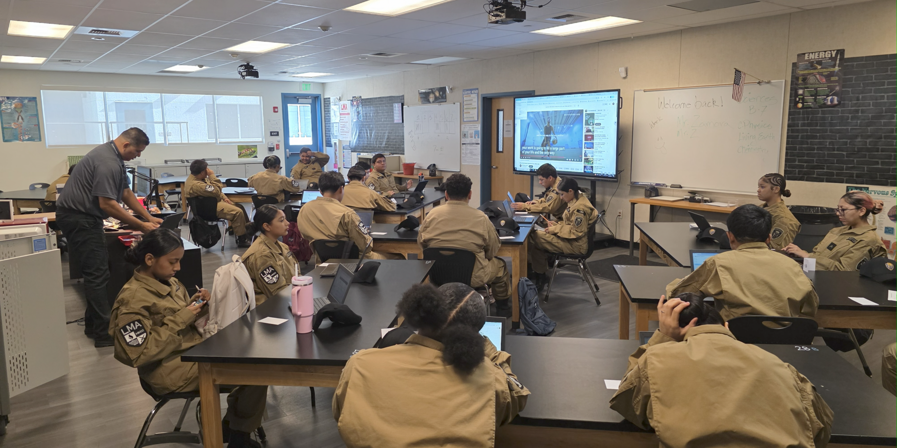 A classroom filled with students in uniforms, focused on a computer presentation.