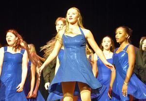 Group of dancers in blue dresses performing on stage.