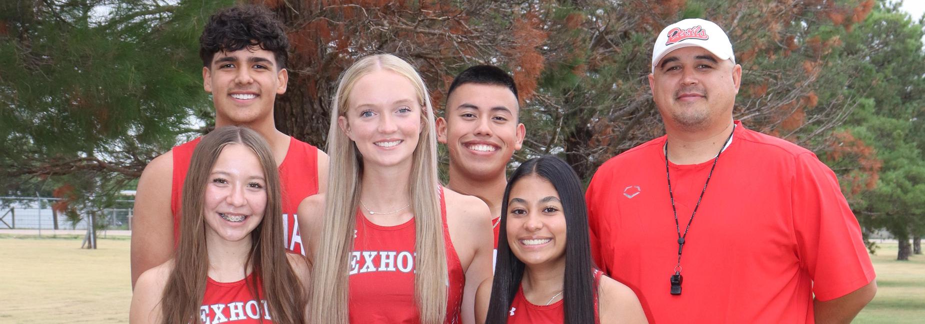 Three female athletes in red uniforms and a coach pose for a photo in a grassy area.