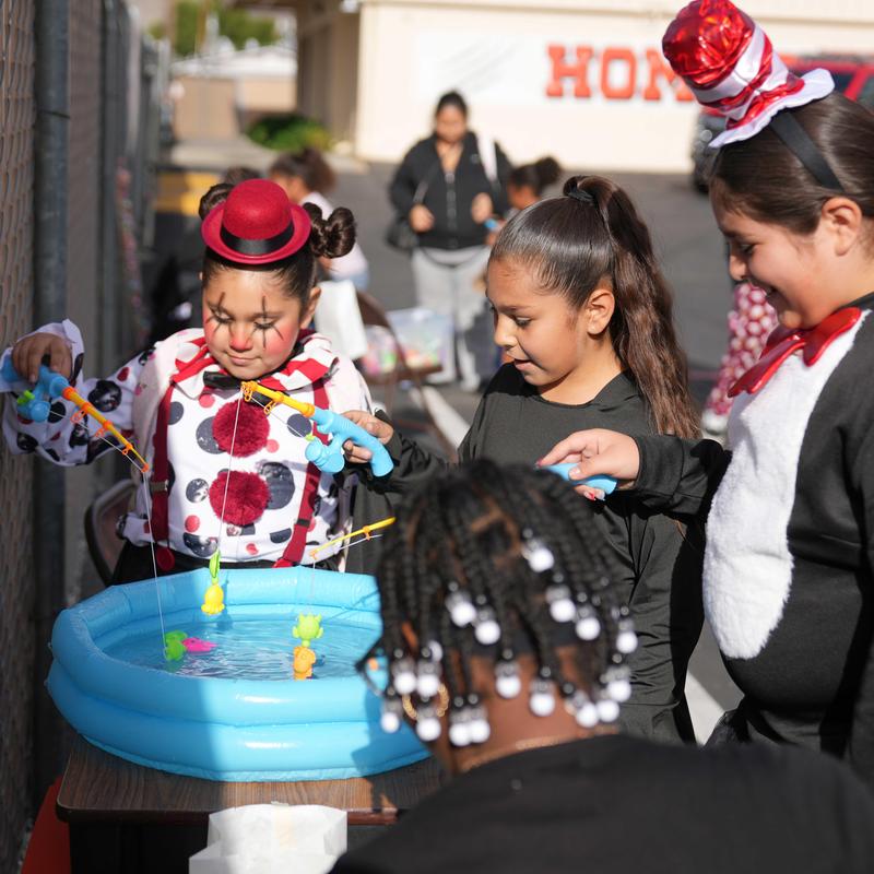 three students dressed in costumes play a fishing game.
