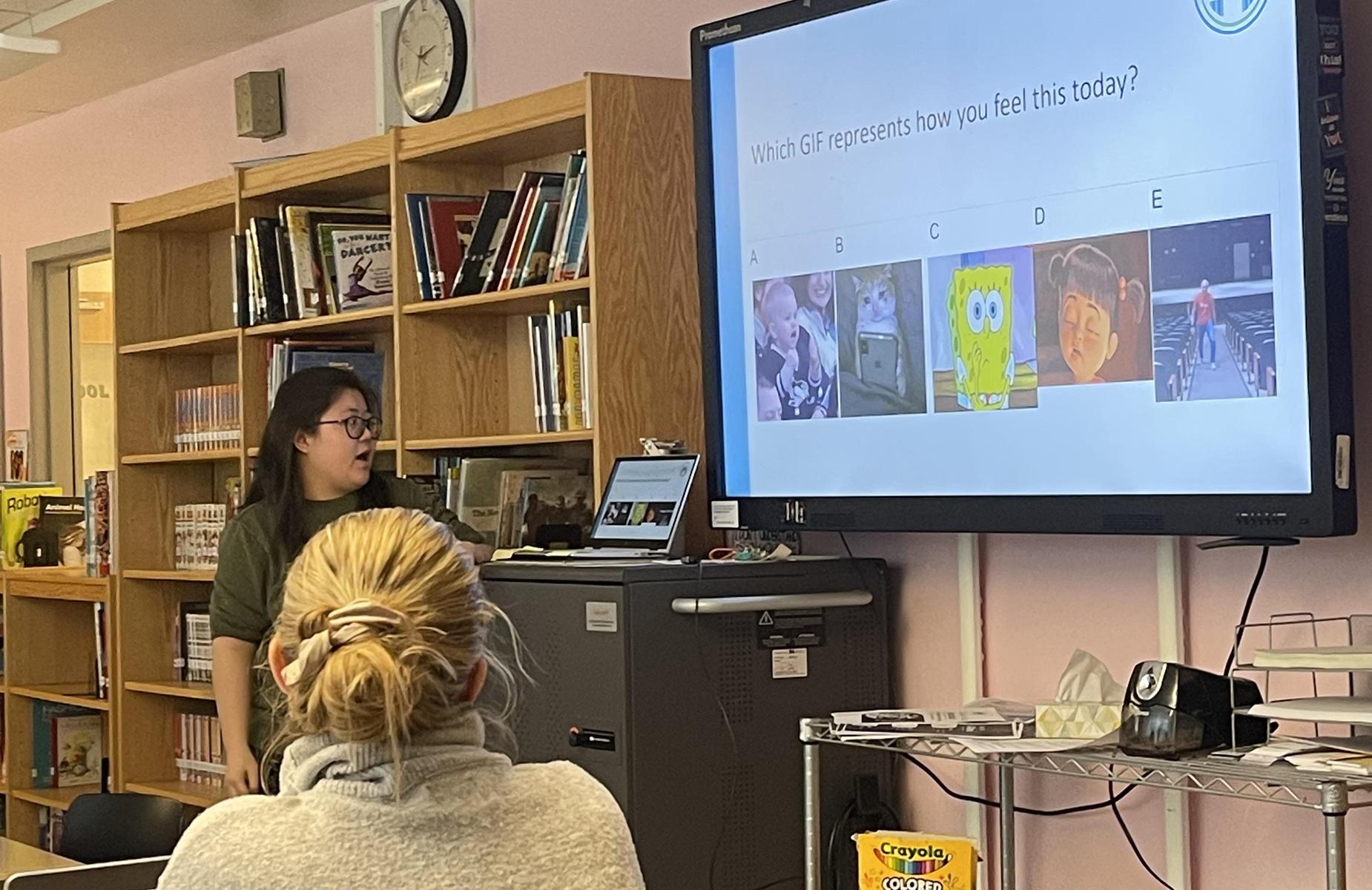 A teacher presents a question using a screen with animated GIFs in a library.