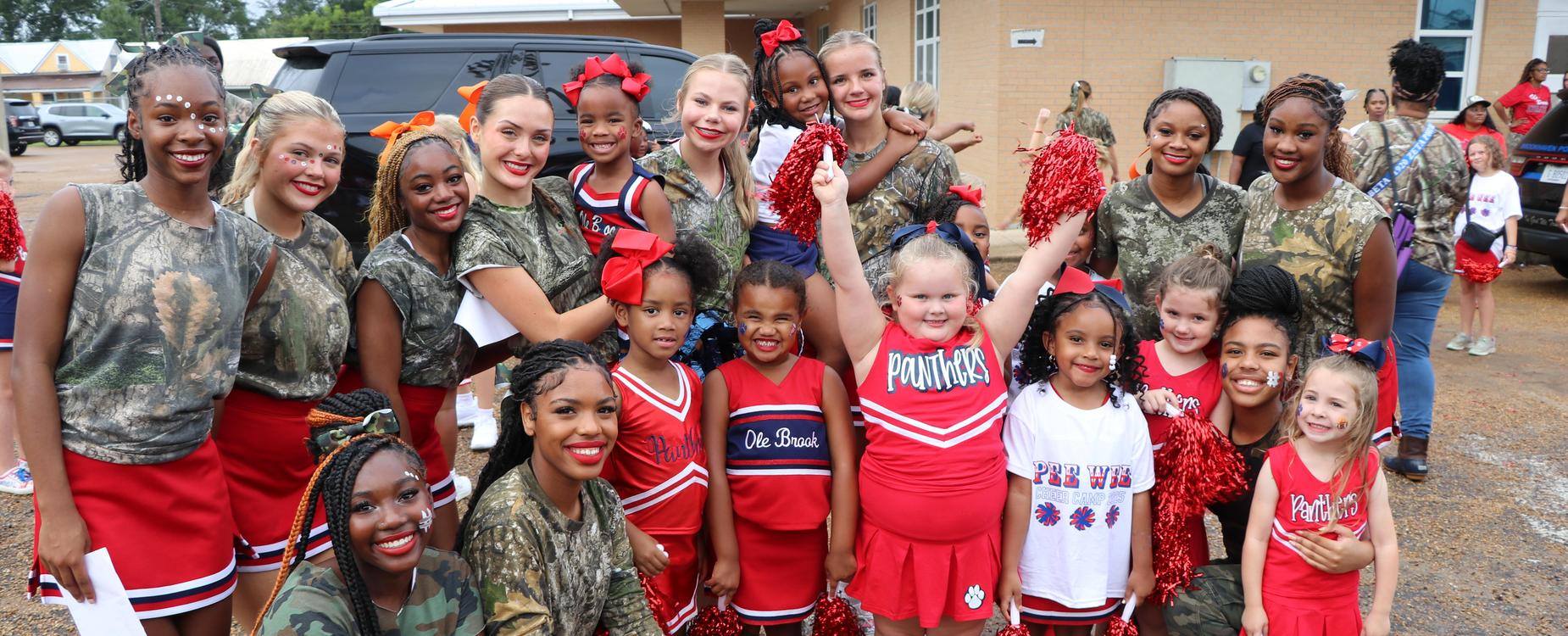 Cheerleaders in matching outfits and camouflage shirts posing happily together at an event.