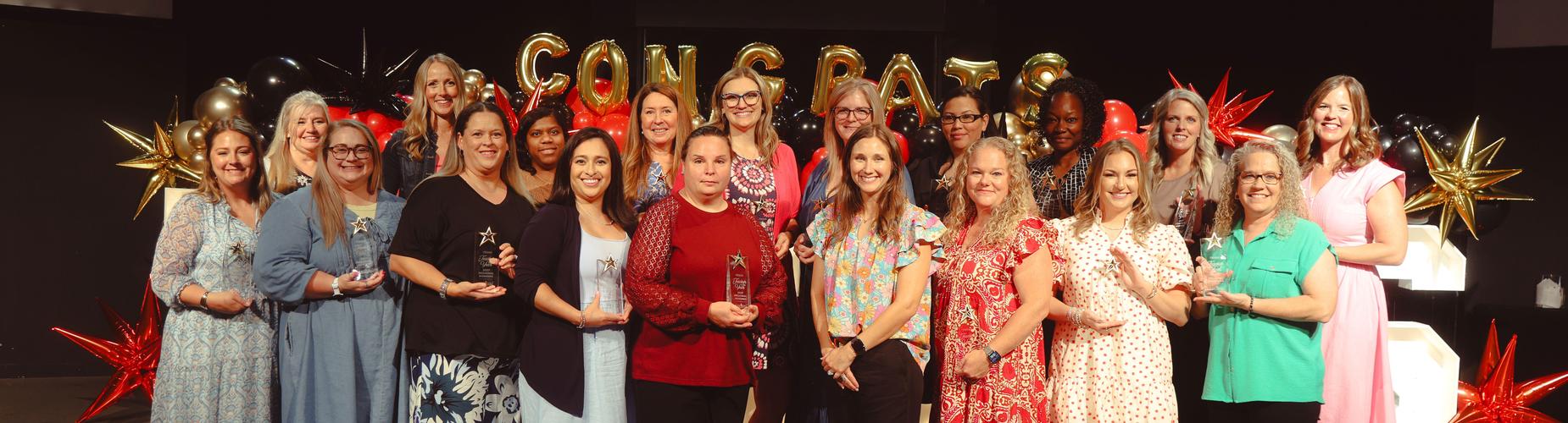 Group of smiling women holding awards at a celebratory event.