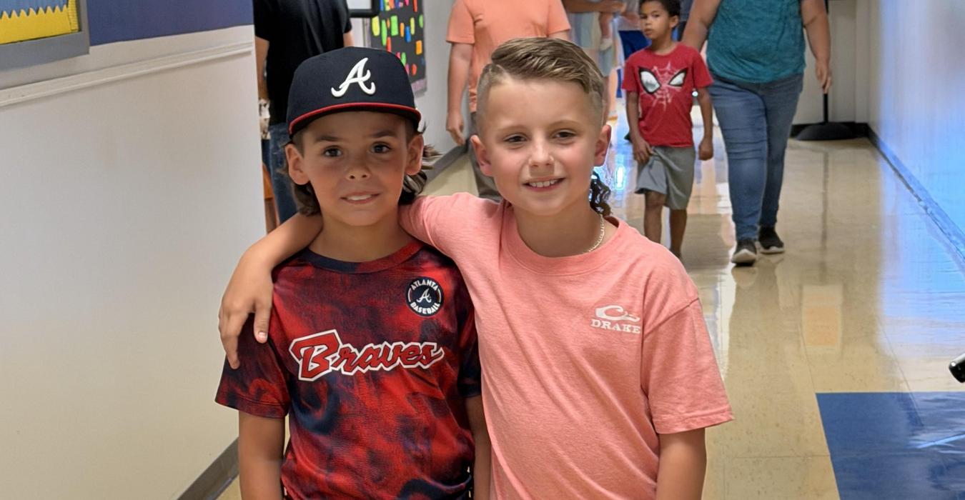 Two boys posing together in a school hallway, smiling.
