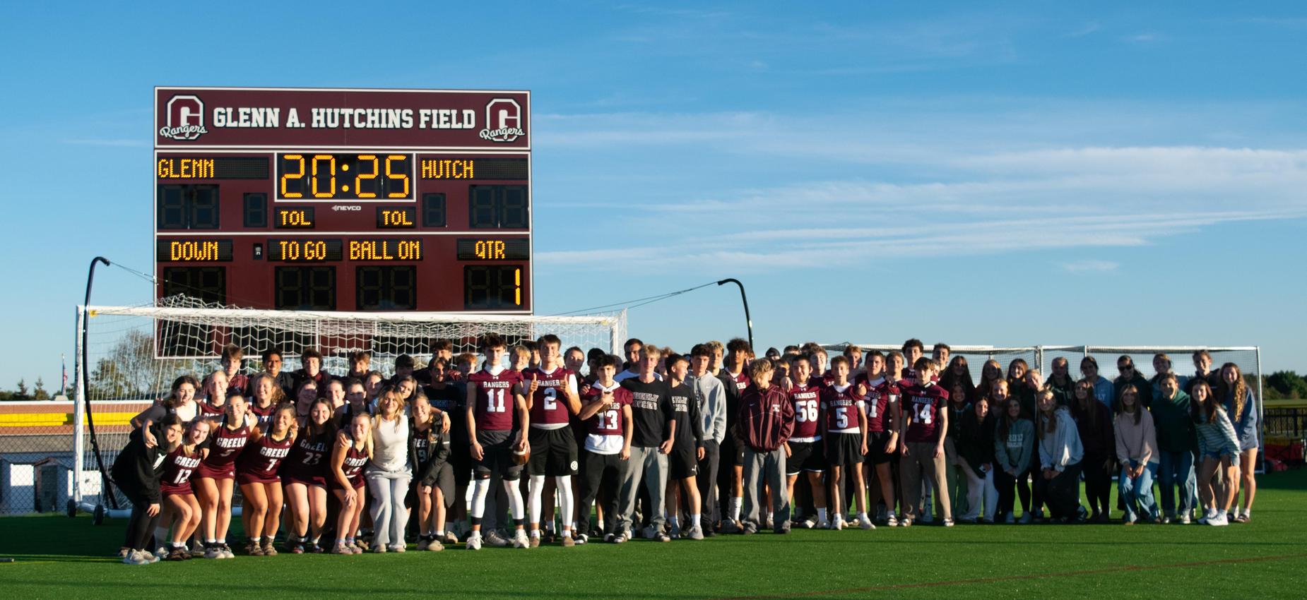 Students and supporters gathered on a football field in front of the scoreboard.
