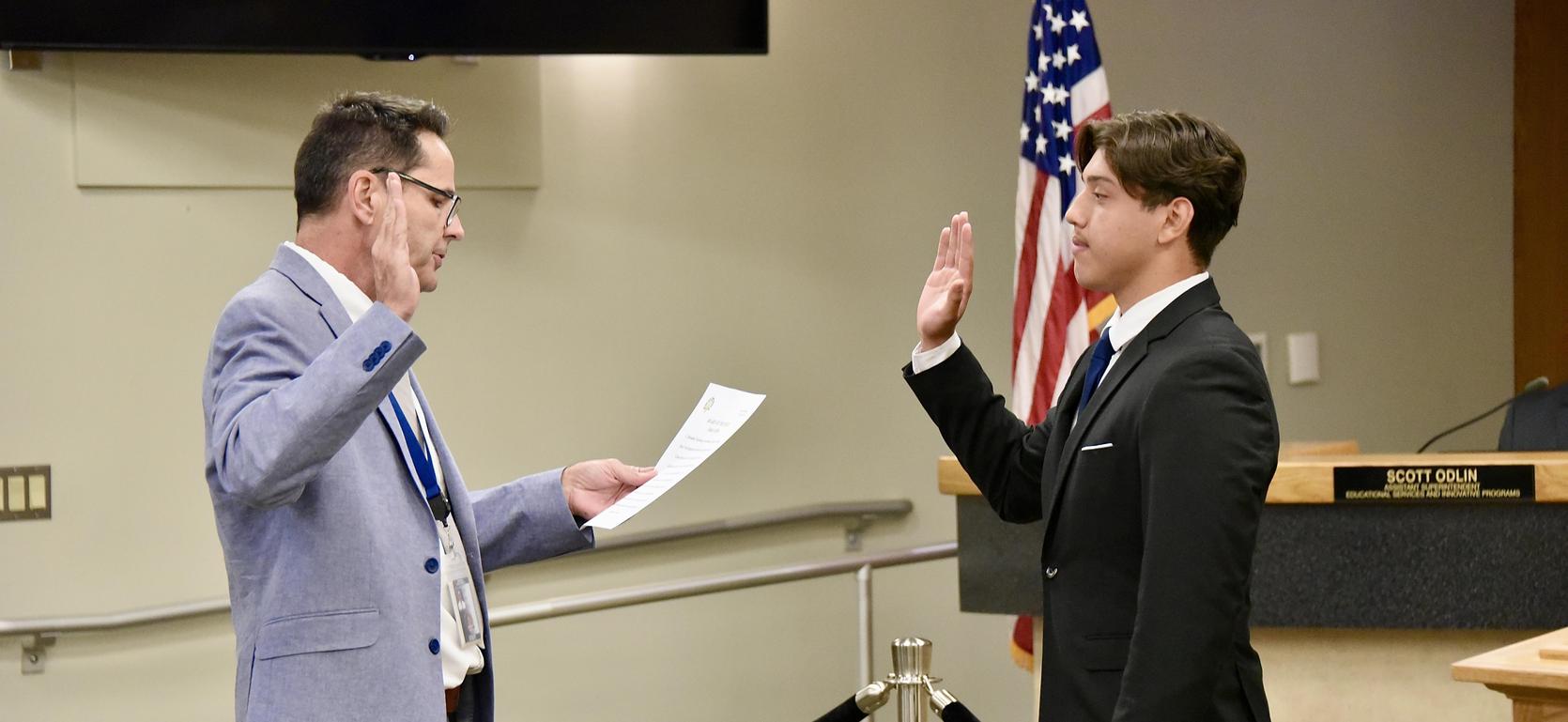 Man administering an oath to a young man in a formal setting.