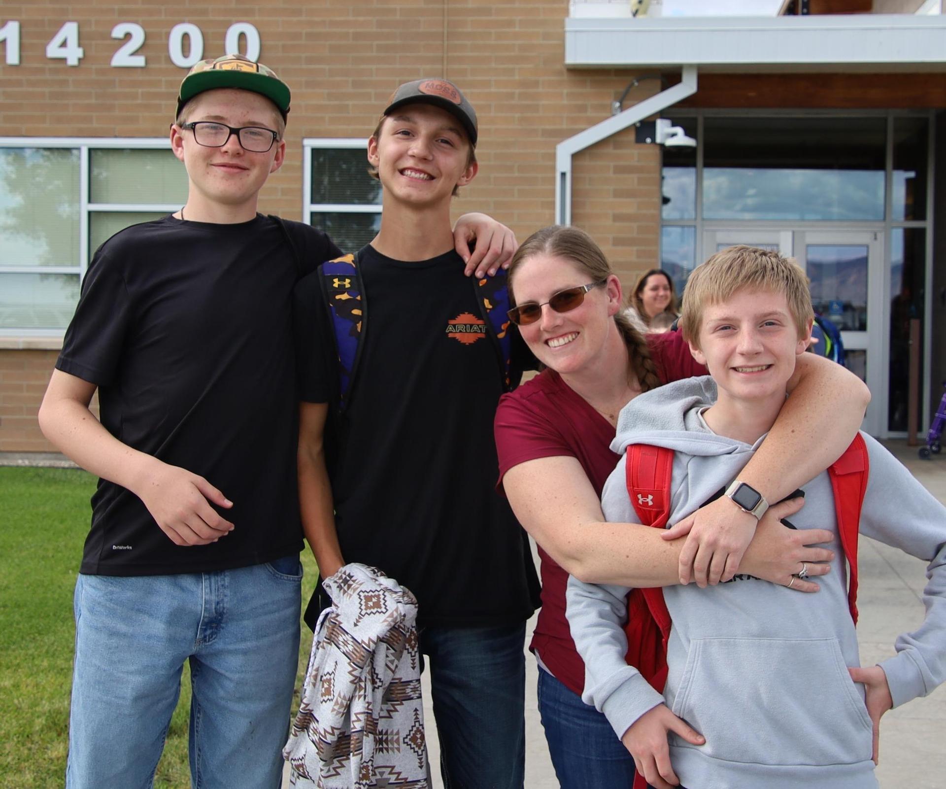 middle school boys and parent smiling at the camera out front of a school