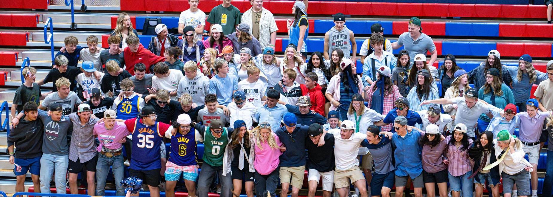 Cheerleaders entertain a lively crowd of students wearing various hats in a gymnasium.