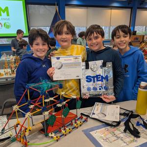 Four male students smile surrounding their K'Nex prototype at the STEM Design Challenge. They are holding their second place certificates.