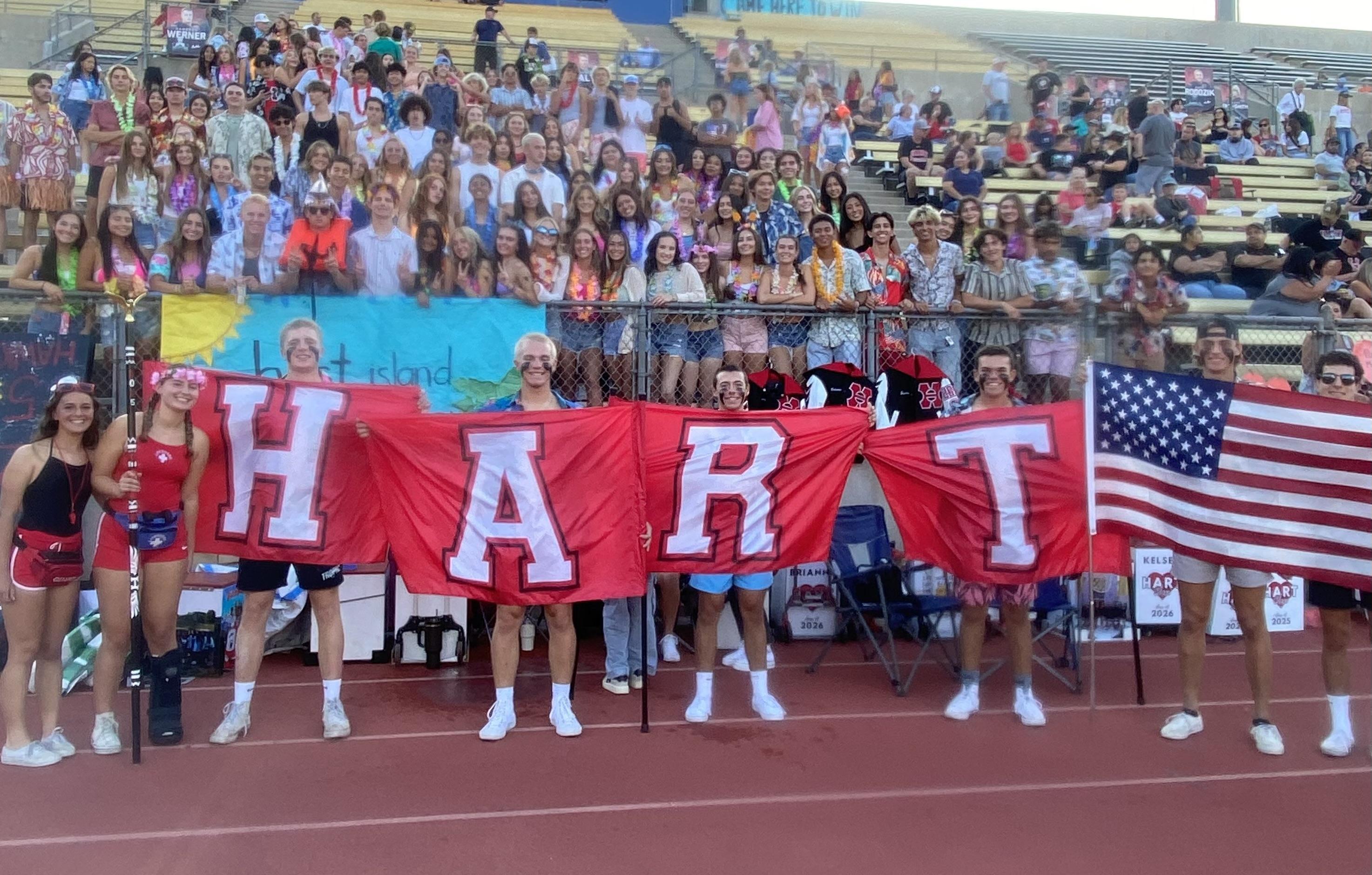Students at a school football game holding red, white, and black banners that spell out HART