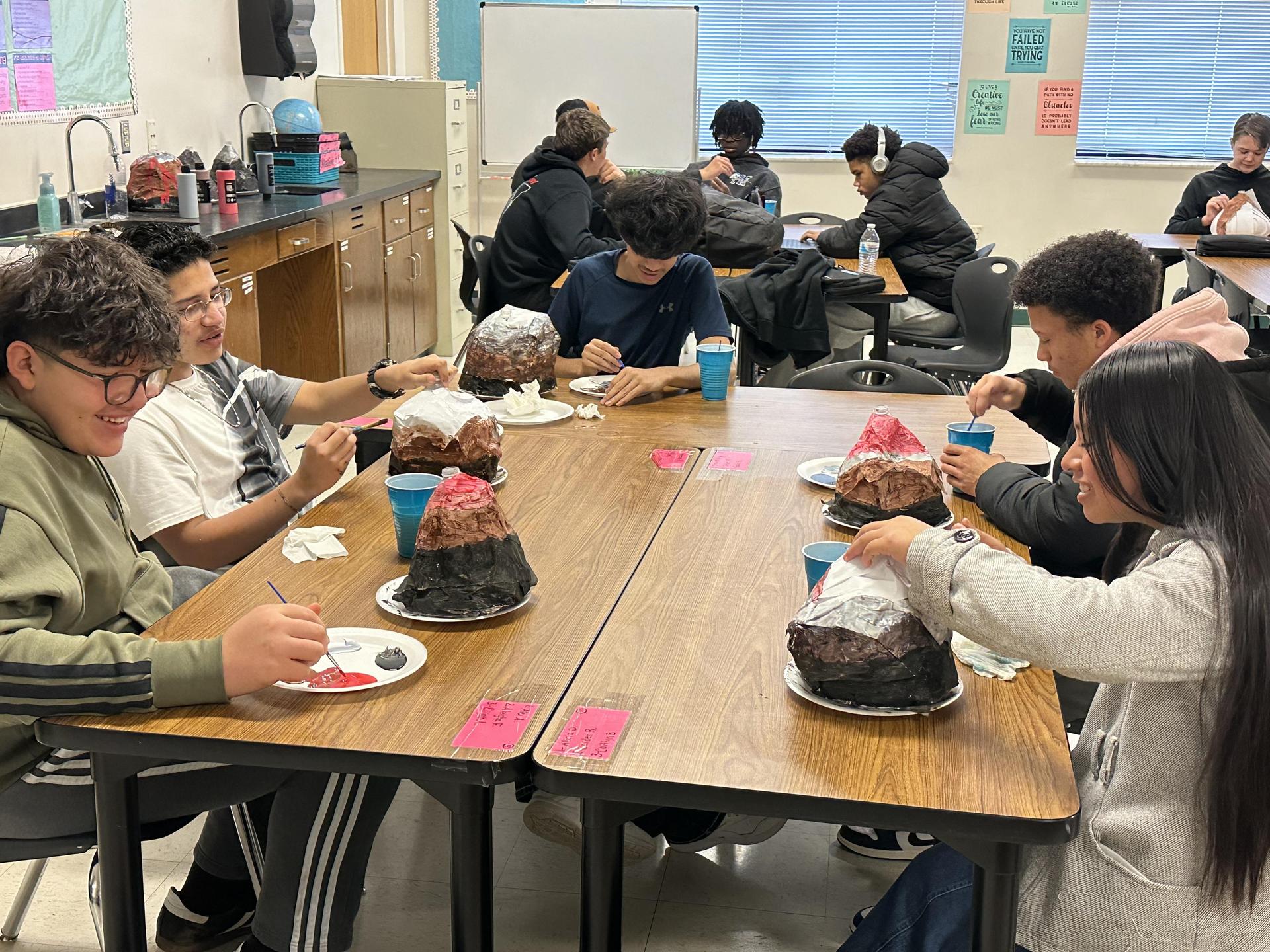 Students decorate volcano models at a classroom table.