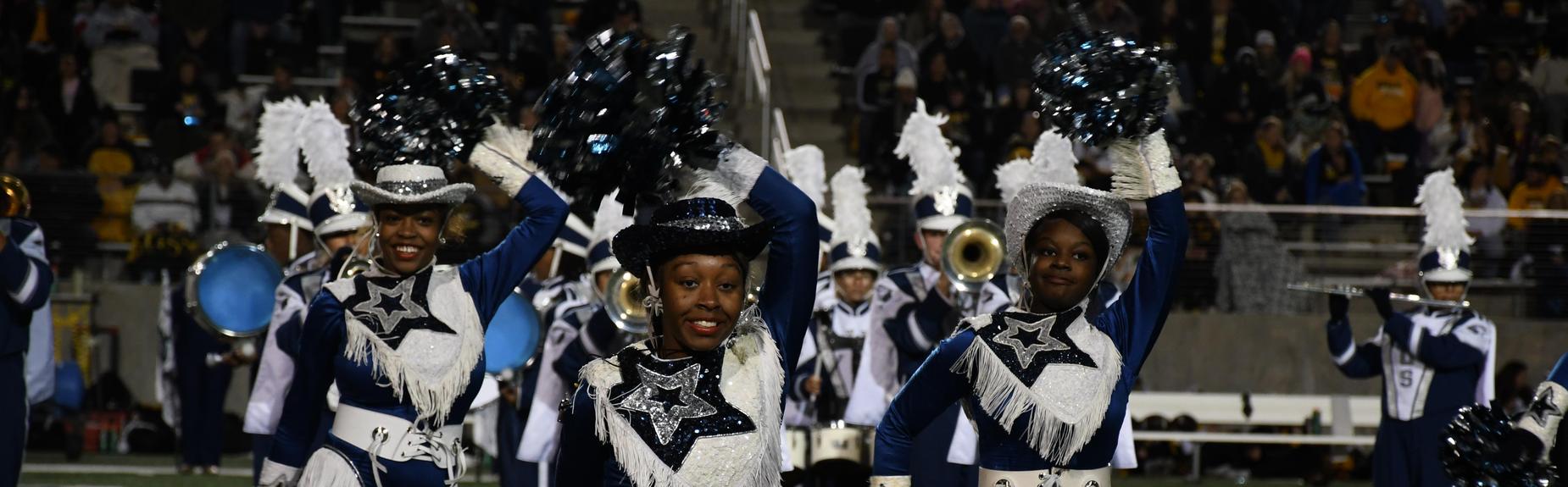 Marching band members and dancers perform together in coordinated outfits on the field.