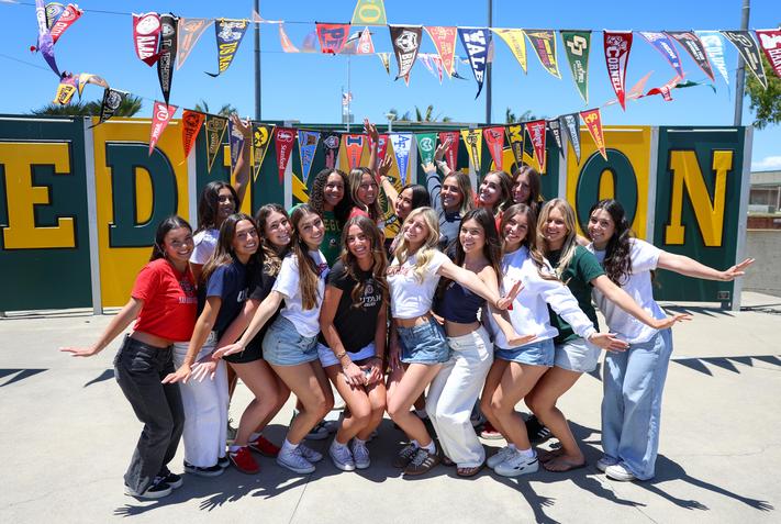 female students posing under various college flags on commitment day
