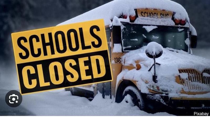 School bus covered in snow with a sign stating 'Schools Closed'.