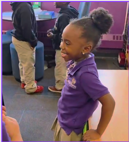 A scholar stands by her desk smiling.