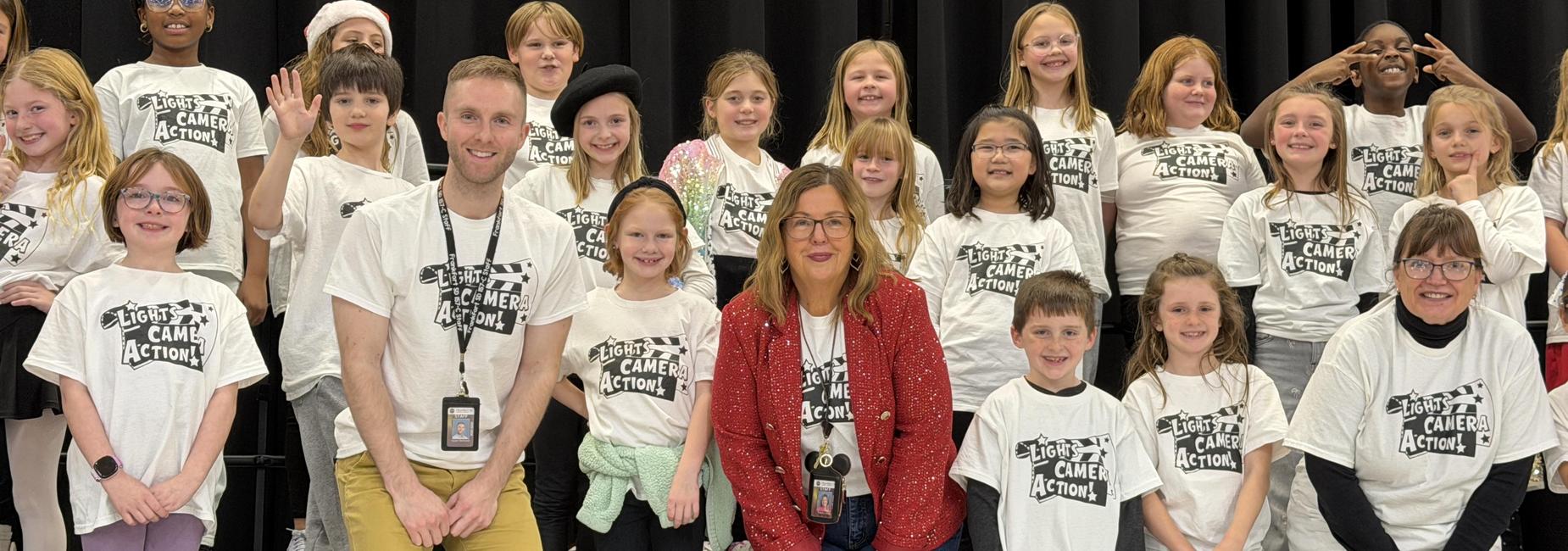 A group of children and adults in matching T-shirts posing for a photo on stage.