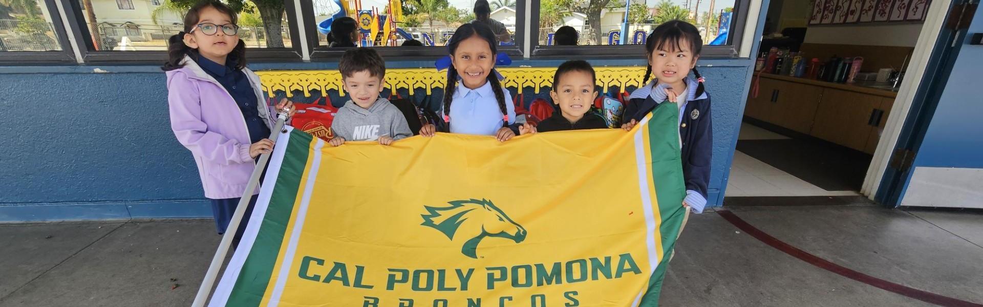Children holding a Cal Poly Pomona Broncos flag outside a building.