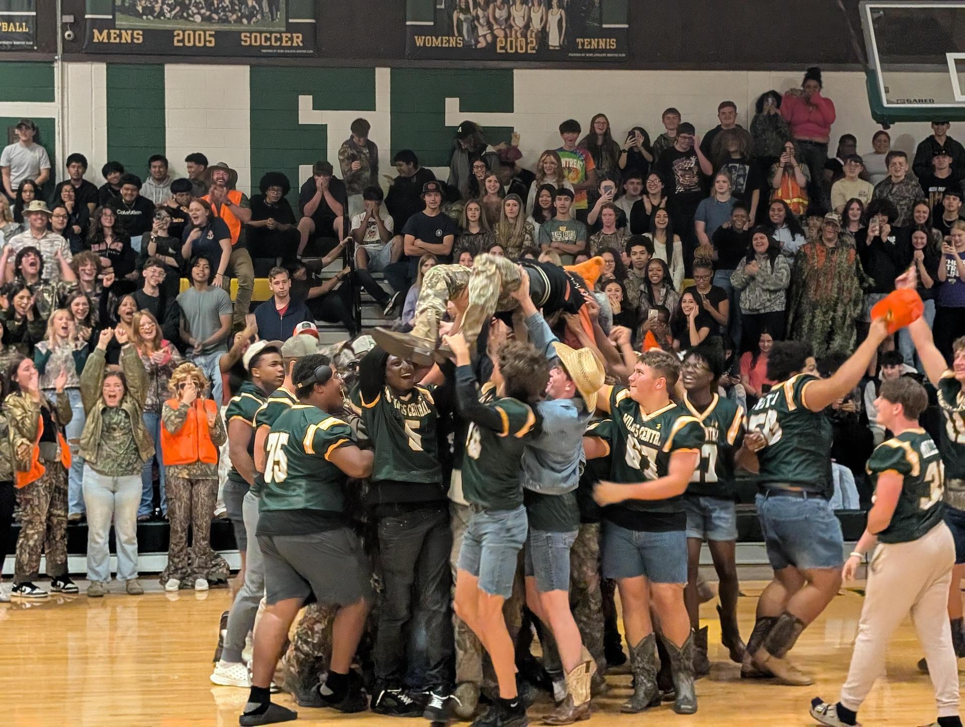 Students joyfully lift a teammate in celebration during a spirited school assembly.