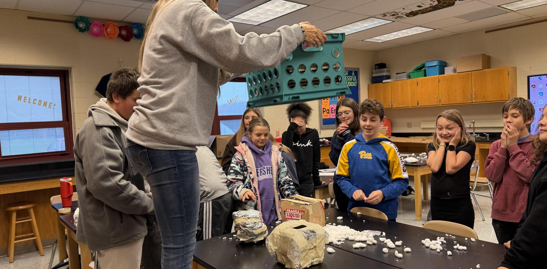 Group of students surprised and engaged while observing a demonstration with crafting materials.