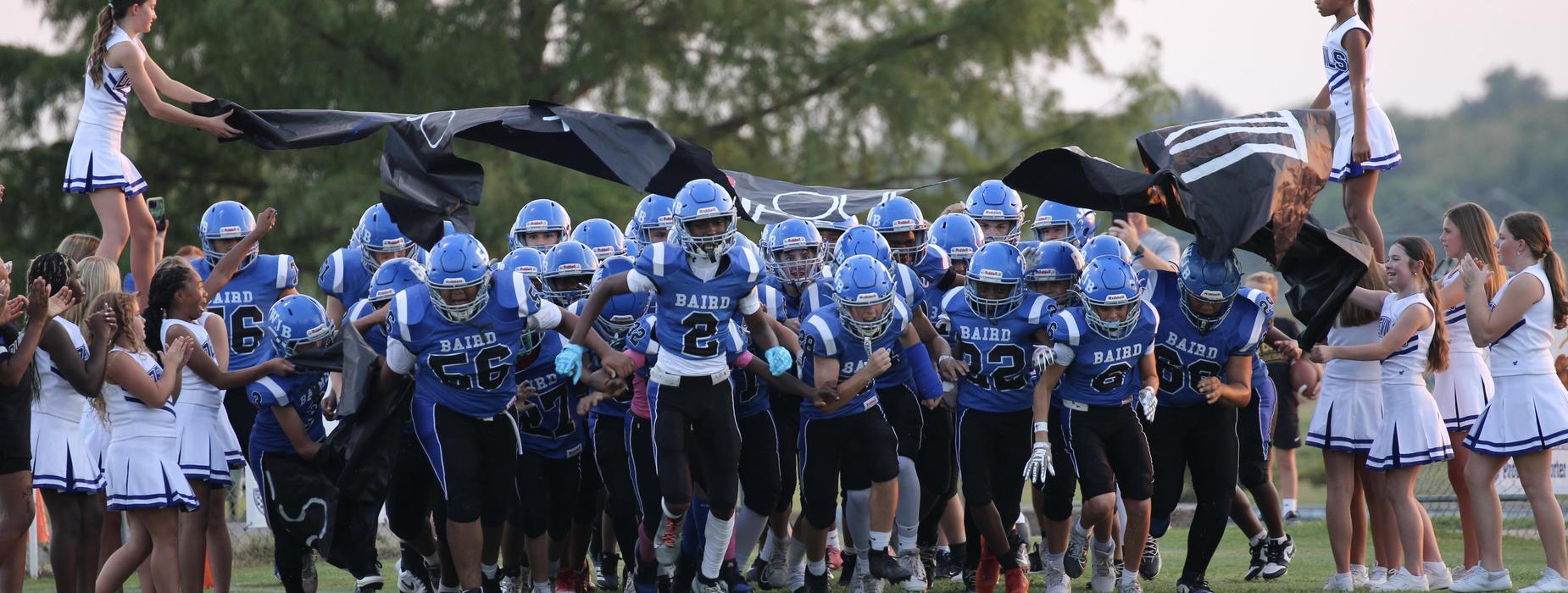 Football team running onto the field, cheered on by cheerleaders.