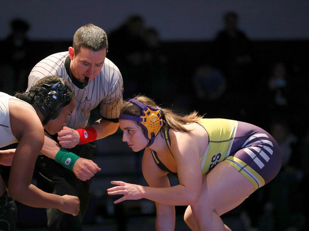 Two wrestlers square off with a referee looking on.
