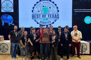 Robotics students standing with trphy in front of Best of Texas Robotics sign