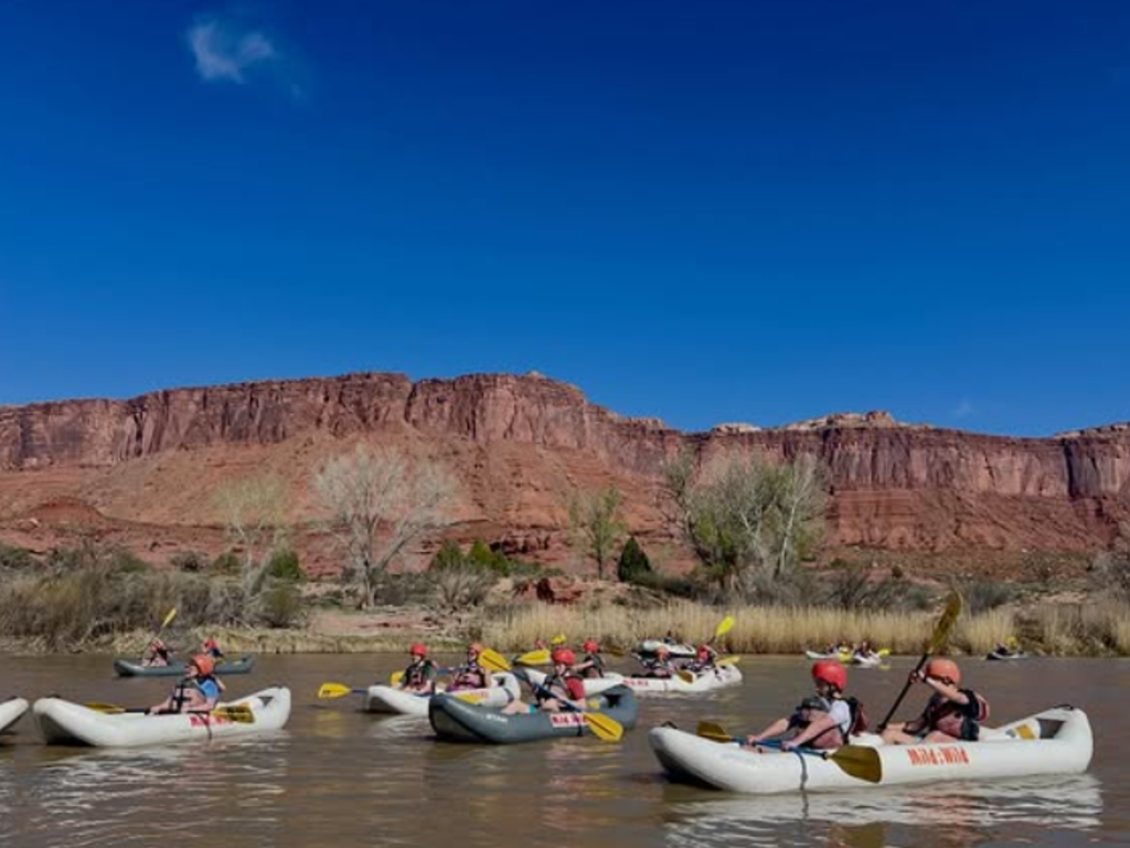 Students kayaking on a river with red mountains in the background.