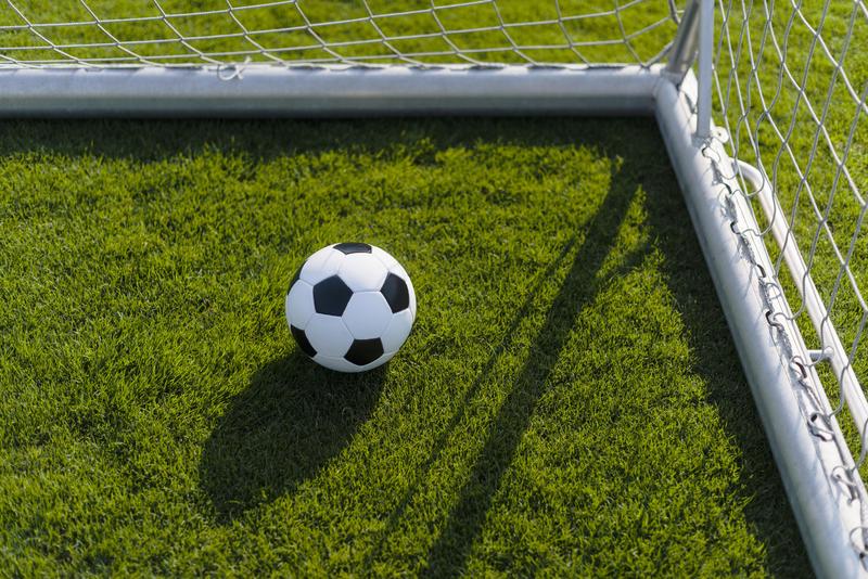 A soccer ball rests on the grass near the corner of a goalpost.
