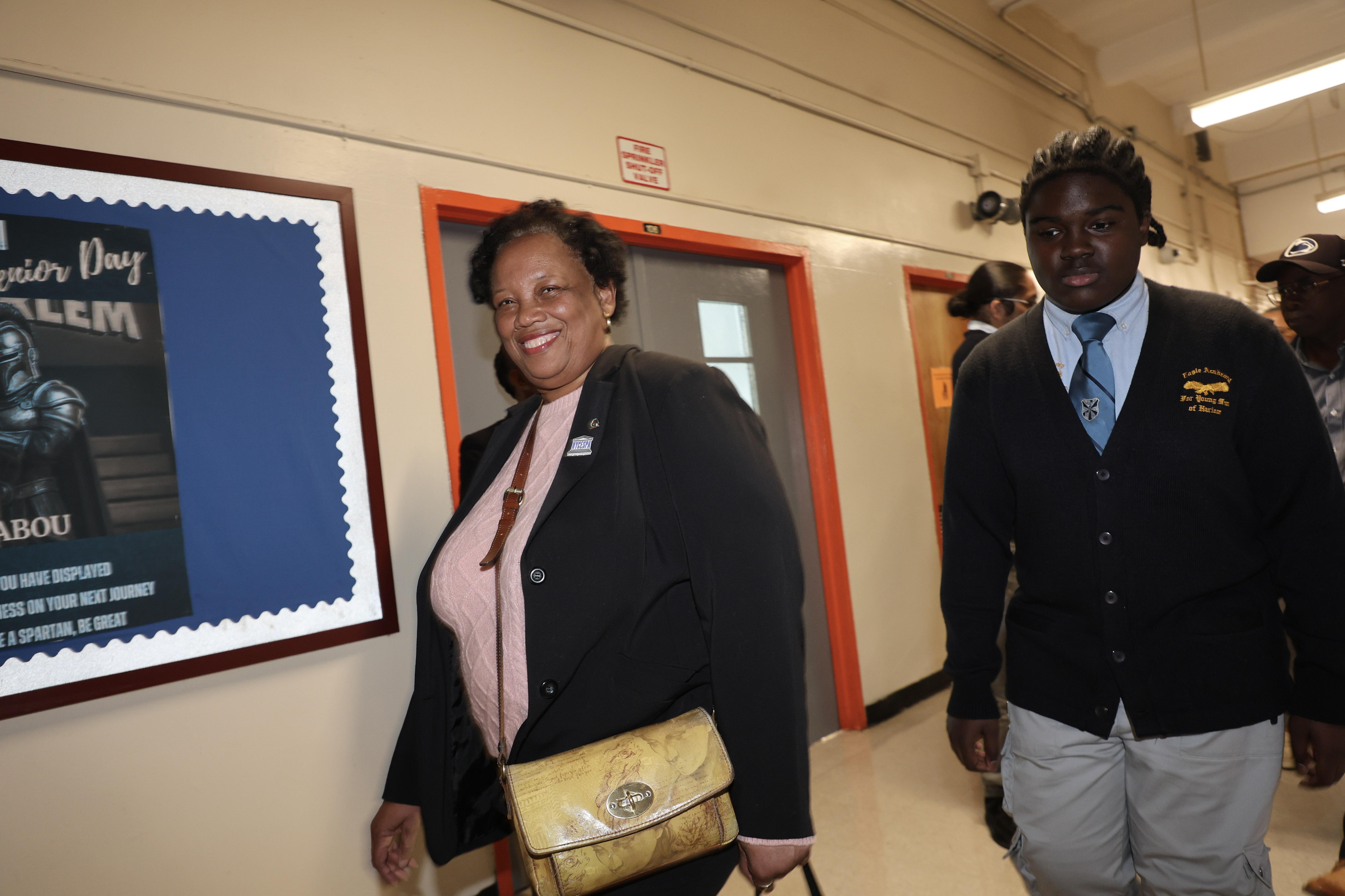 A smiling woman and a young man walking in a school hallway with a poster.