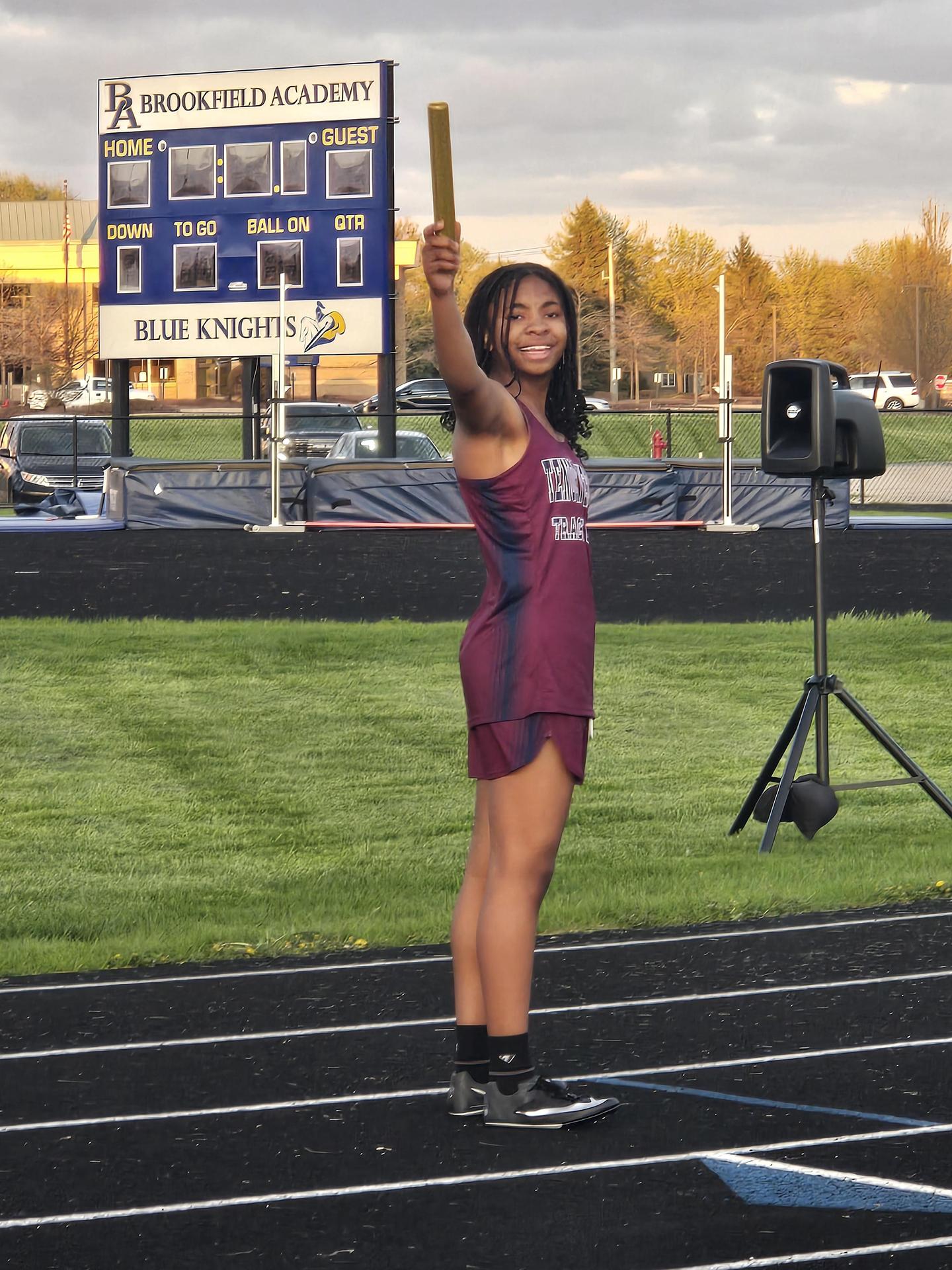 A trach athlete holding the relay baton and smiling at the camera.
