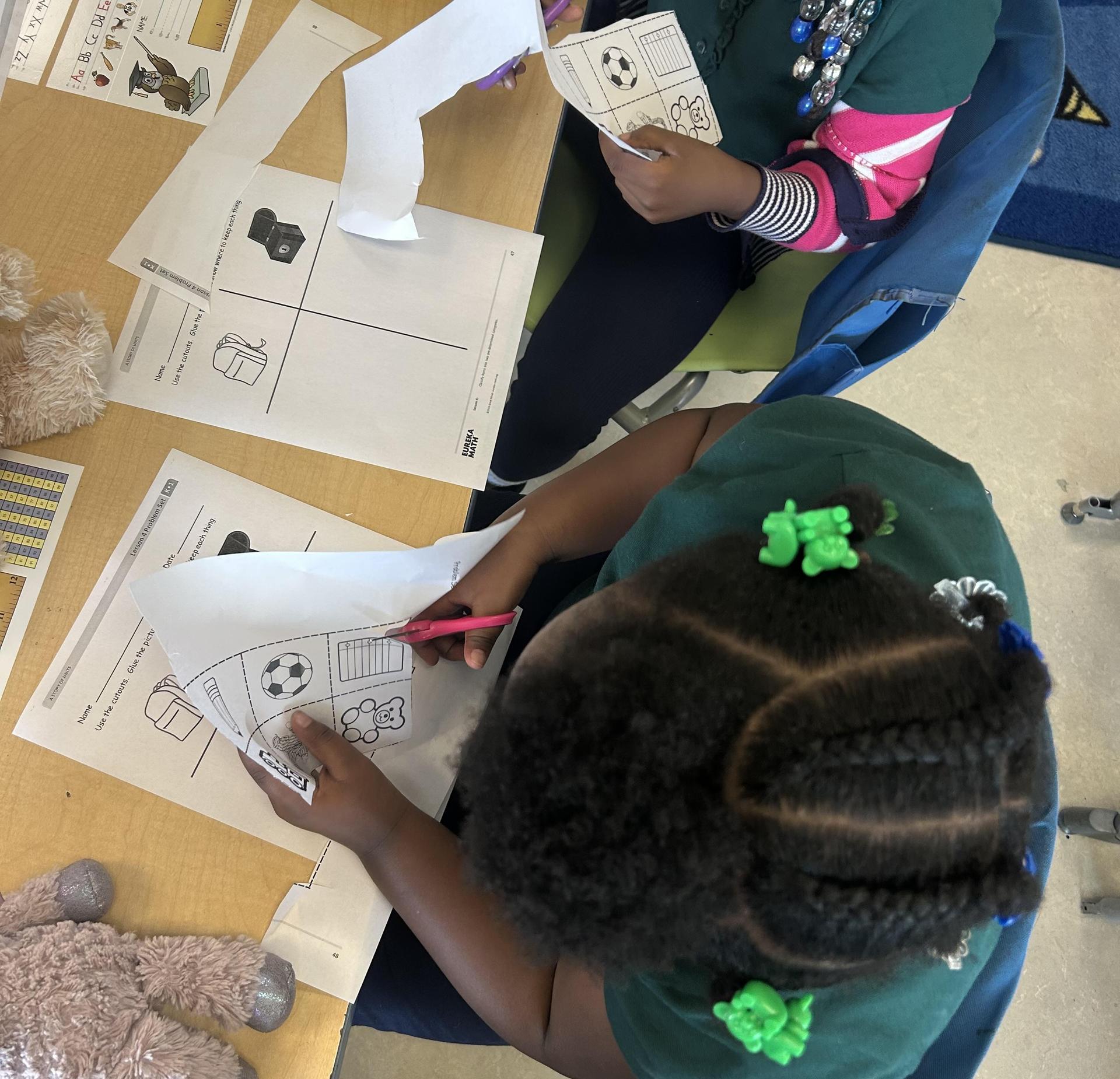 Two children working on a worksheet at a table with toys nearby.