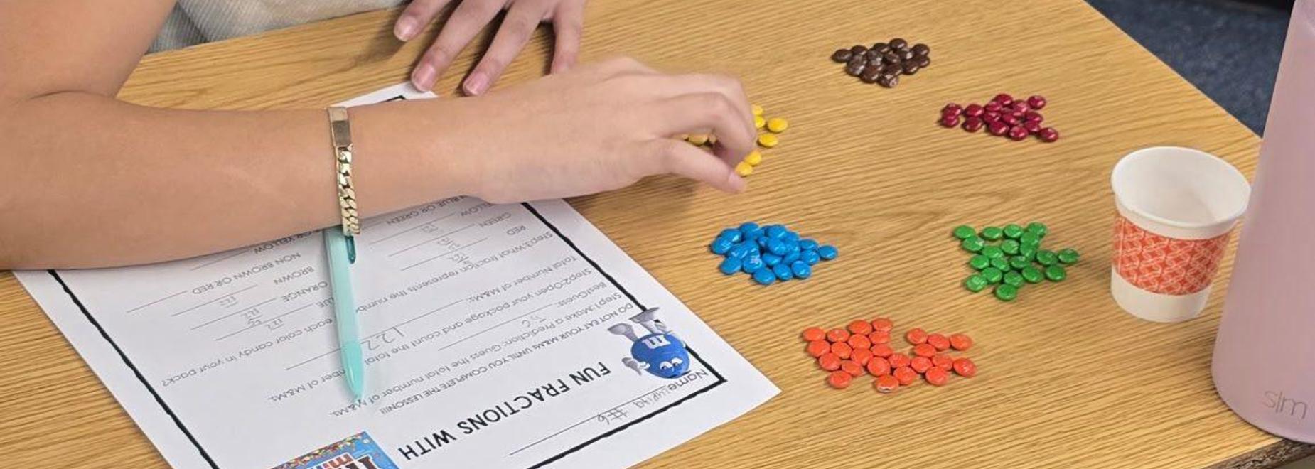 Student sorting colored candies on a worksheet at a table.