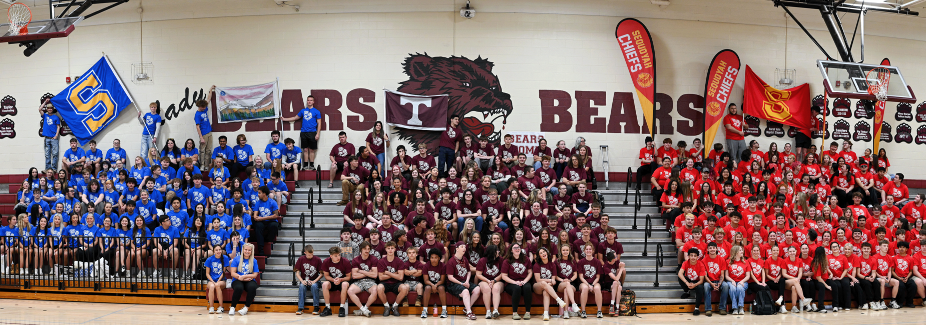 Students in blue, maroon, and red shirts gathered in a gym, representing different teams.
