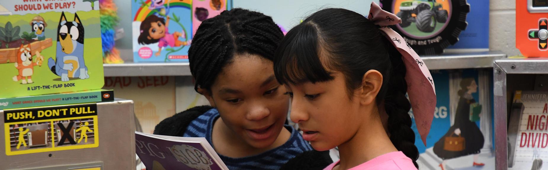 Two children reading a book together in a colorful library setting.