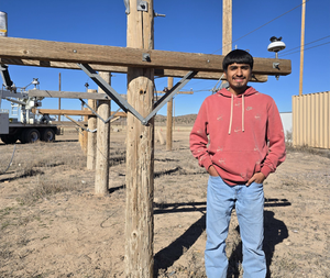 Image of young adult male student in a hoodie and jeans in front of an electrical line post
