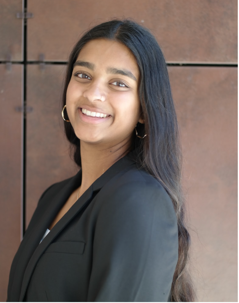 A young woman in a black blazer smiling in front of a textured background.