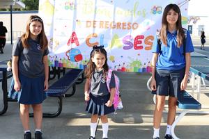 three students in front of a Spanish sign on the first day of school