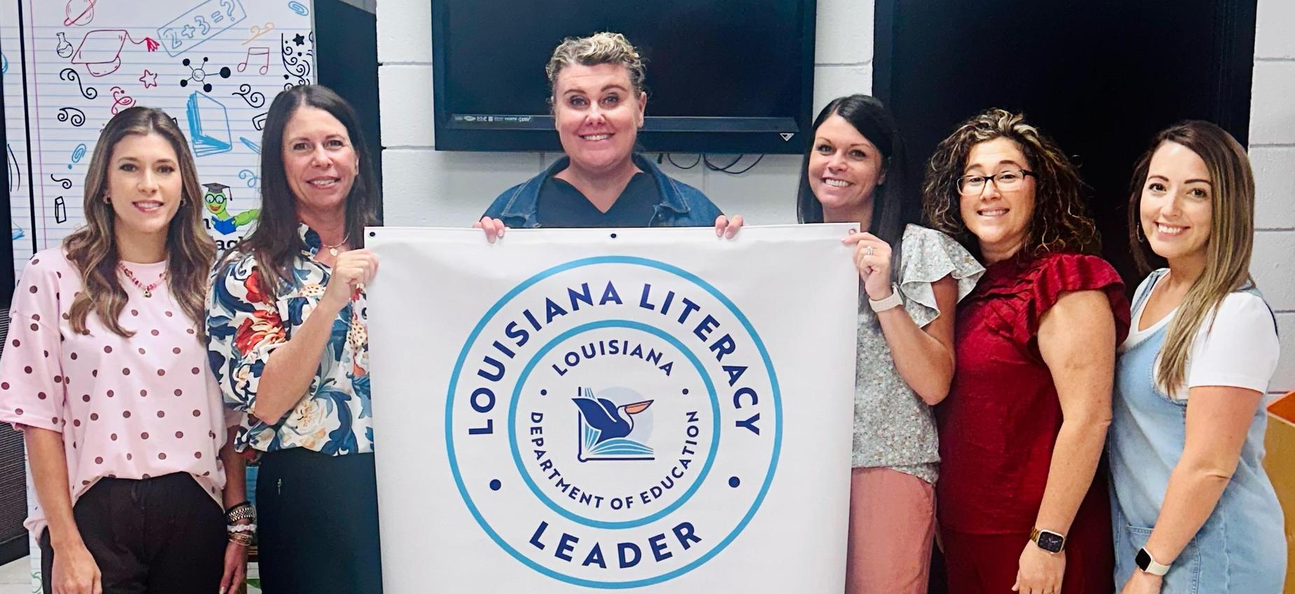 Group of six women smiling around a literacy achievement banner in Louisiana.