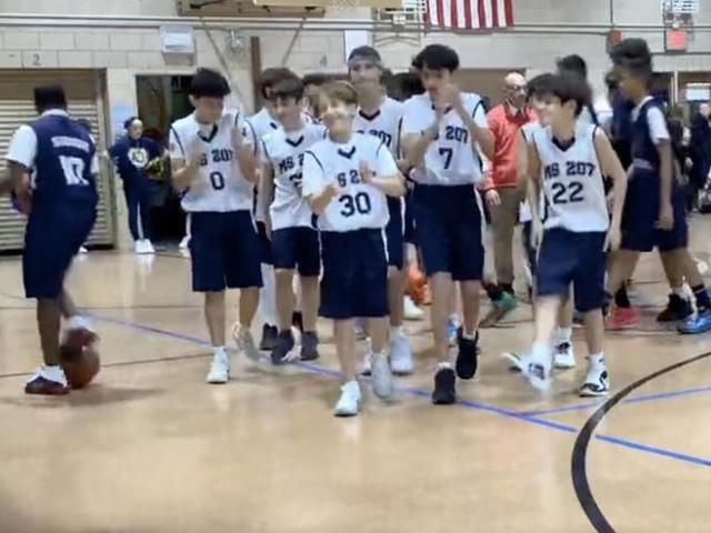 Group of boys in sports jerseys walking on a basketball court.