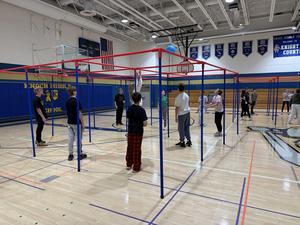 Students standing on a gym floor under a 9 square gym equipment