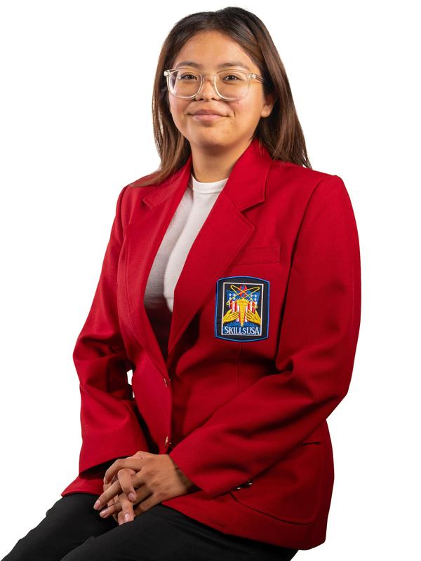 A young woman in a red blazer with an emblem, smiling at the camera.